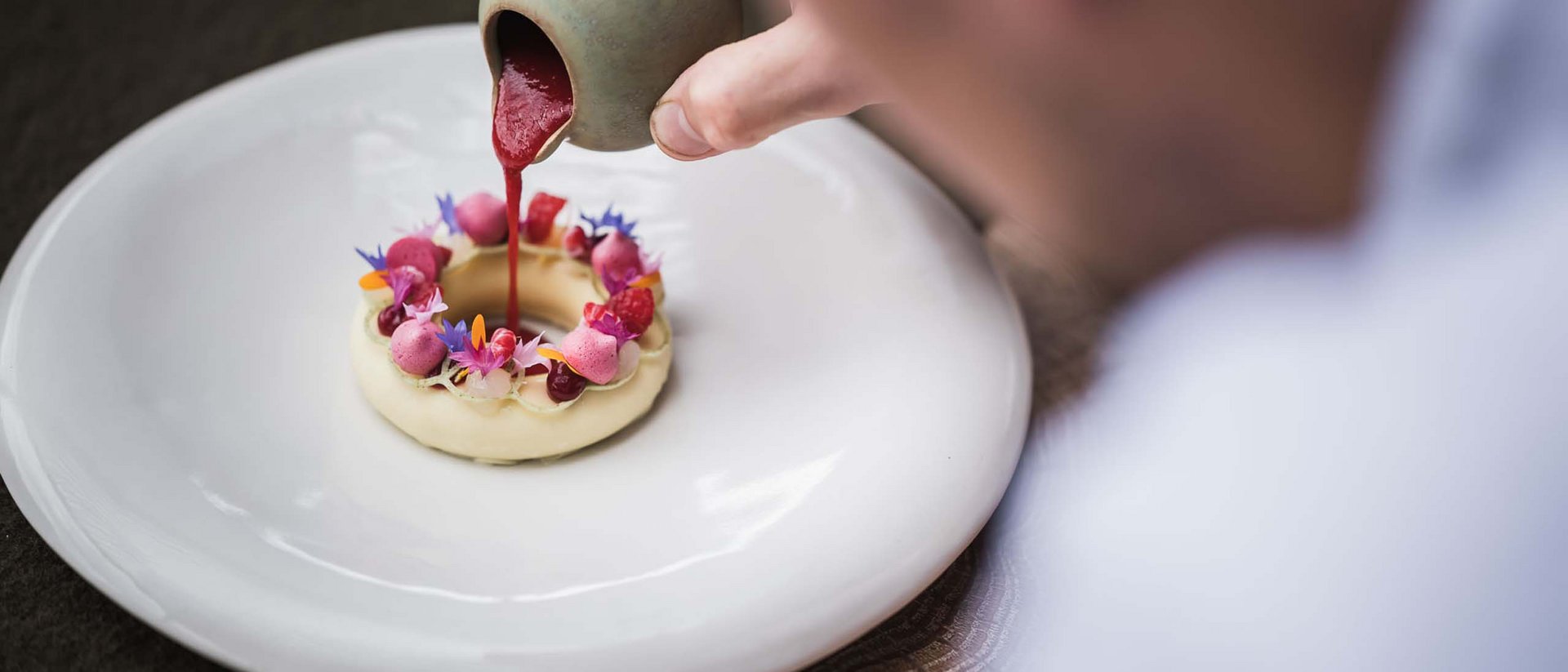 An enriching holiday in your luxury chalet in South Tyrol Hand pouring red sauce on artistically decorated dessert on white plate