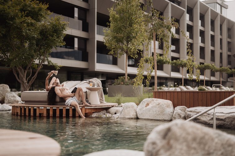 Couple relaxing on lounge chair by water with modern building in background