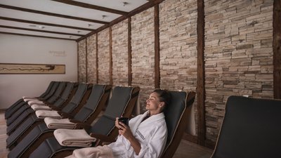 Frau entspannt in Bademantel auf Liegestuhl in Spa mit Steinwand