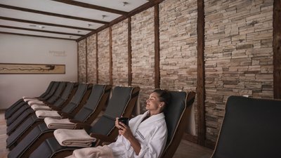 Frau entspannt in Bademantel auf Liegestuhl in Spa mit Steinwand