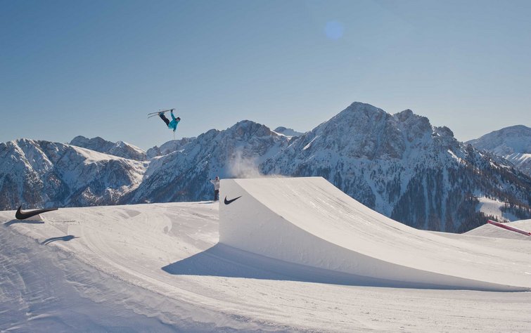 Scialpinista esegue una figura aerea su una pista da snowboard con montagne sullo sfondo