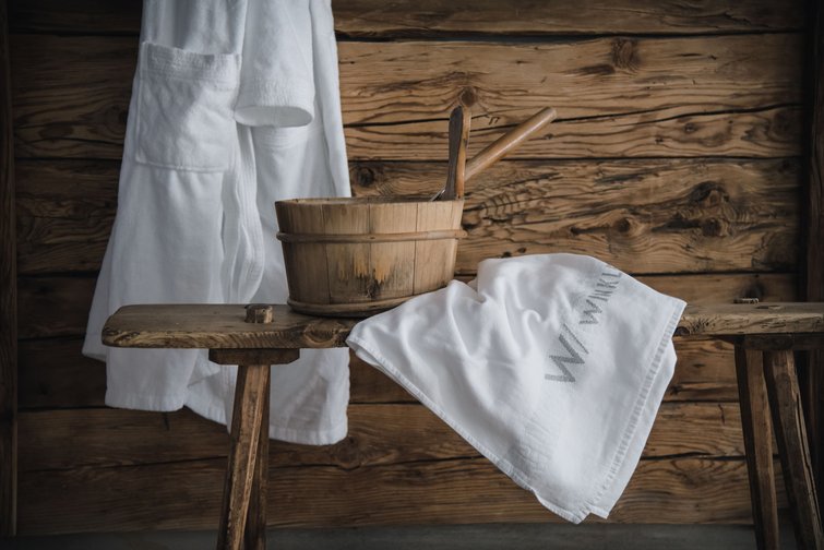 Saunabank mit Holzeimer, Kelle und weißen Handtüchern vor Holzwand