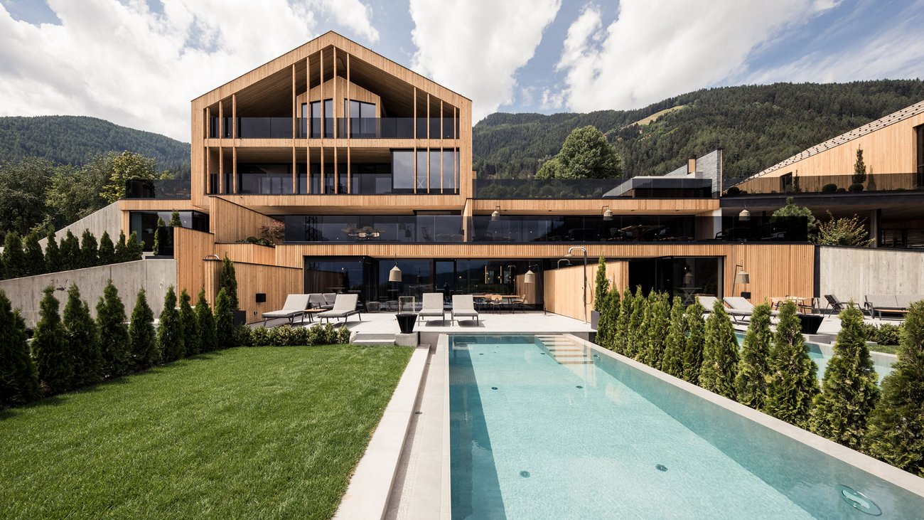 Modern house with wood siding, pool, and mountain view under a partly cloudy sky