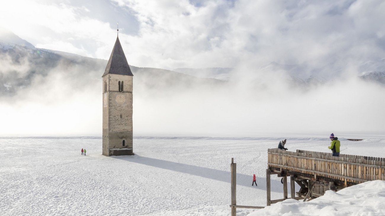 Versunkener Kirchturm ragt aus zugefrorenem und verschneitem See bei Nebel