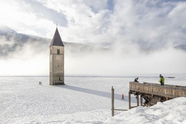 Sunken church tower rising from frozen snowy lake with fog