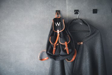 Dark gray backpack and coat hanging on hooks on a gray wall