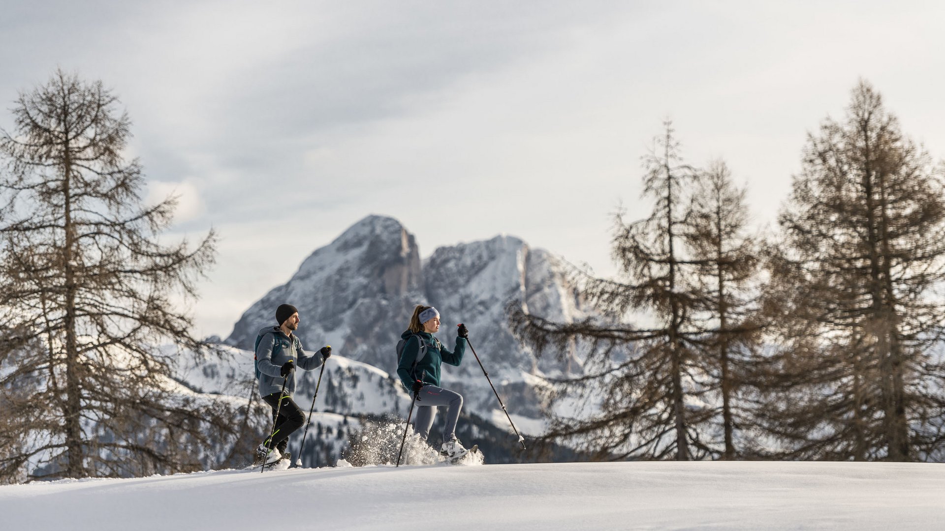 Two people snowshoe hiking in a snowy mountain landscape