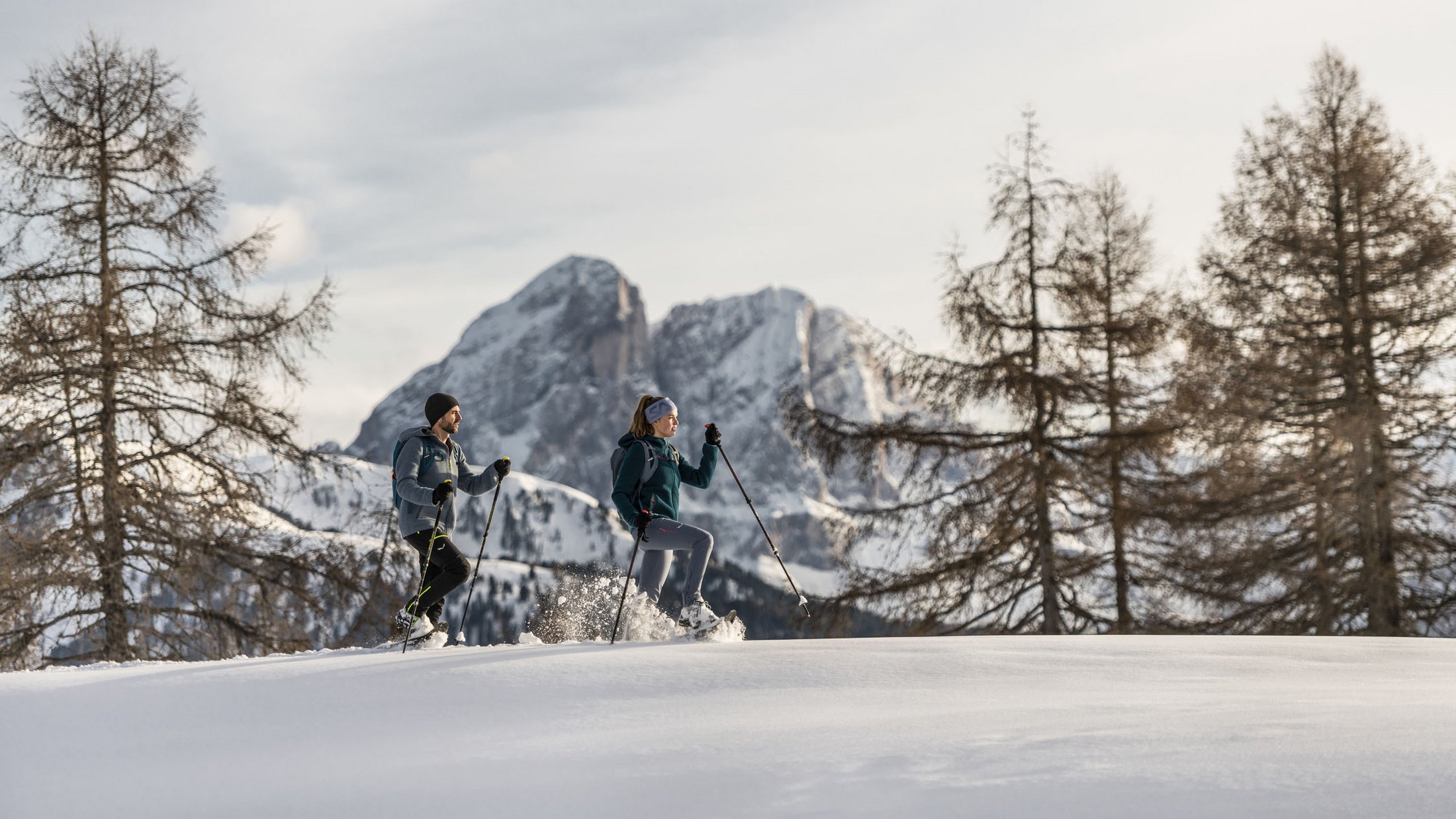 Two people snowshoe hiking in a snowy mountain landscape