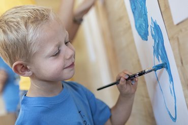 Bambino dipinge felice con colore blu su carta appesa alla parete