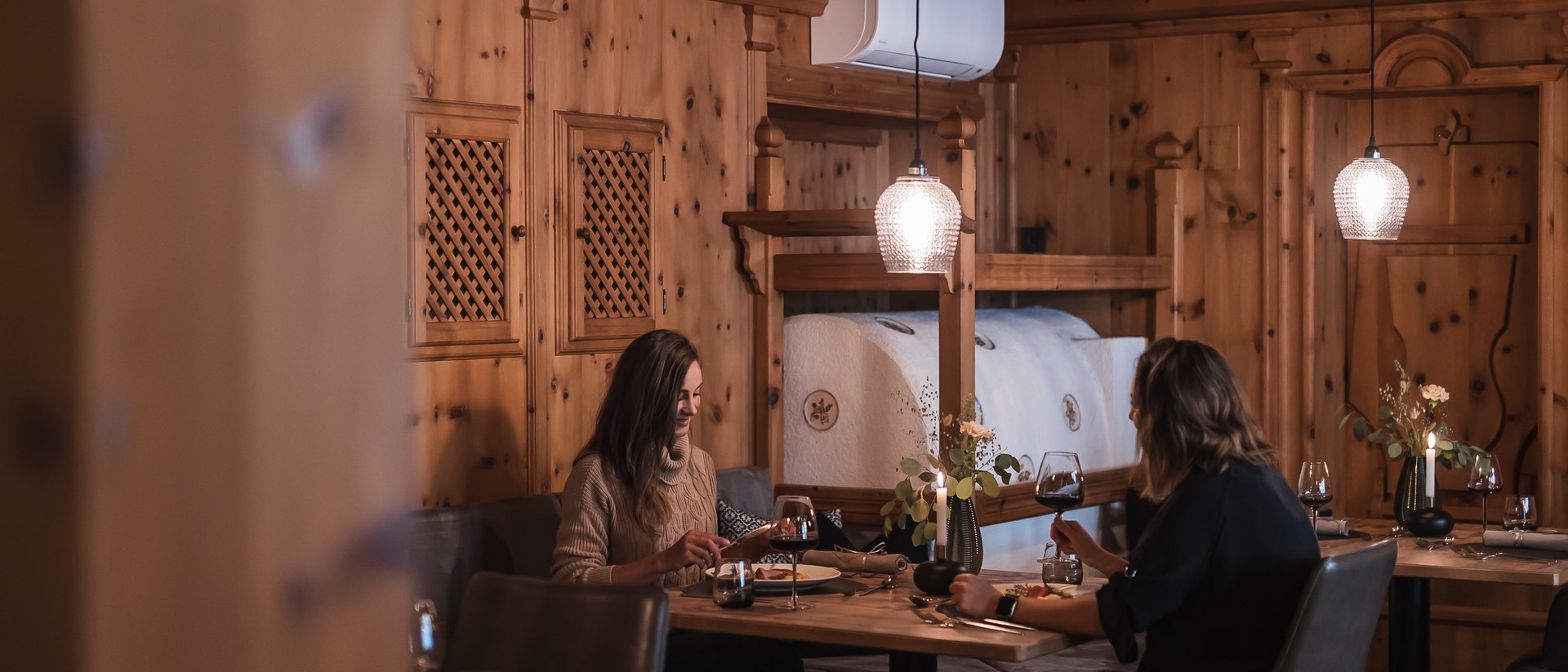 Zwei Frauen essen in gemütlichem Holzrestaurant bei Kerzenlicht