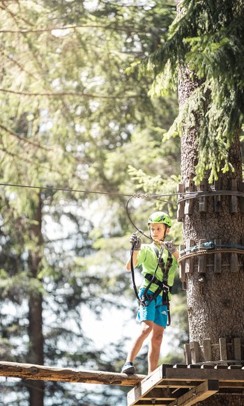 Junge mit Helm beim Klettern im Hochseilgarten
