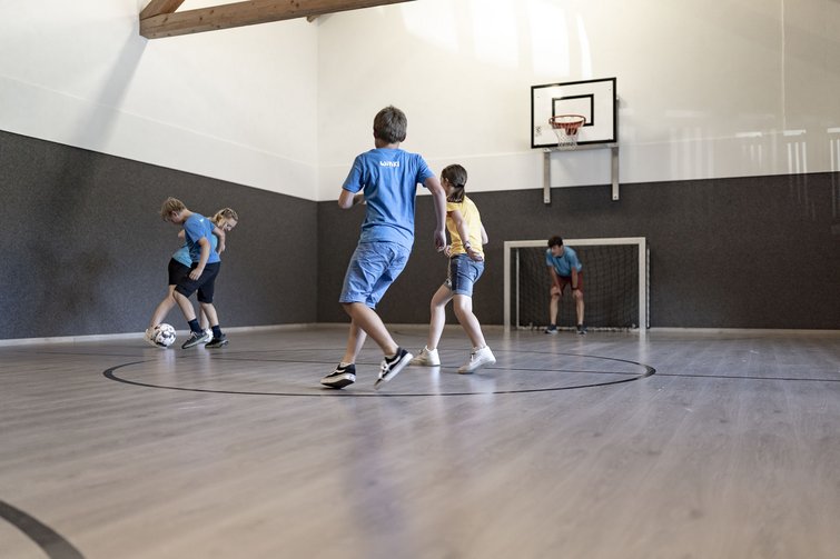 Kinder spielen Fußball in einer Indoor-Sporthalle mit Basketballkorb und Tor