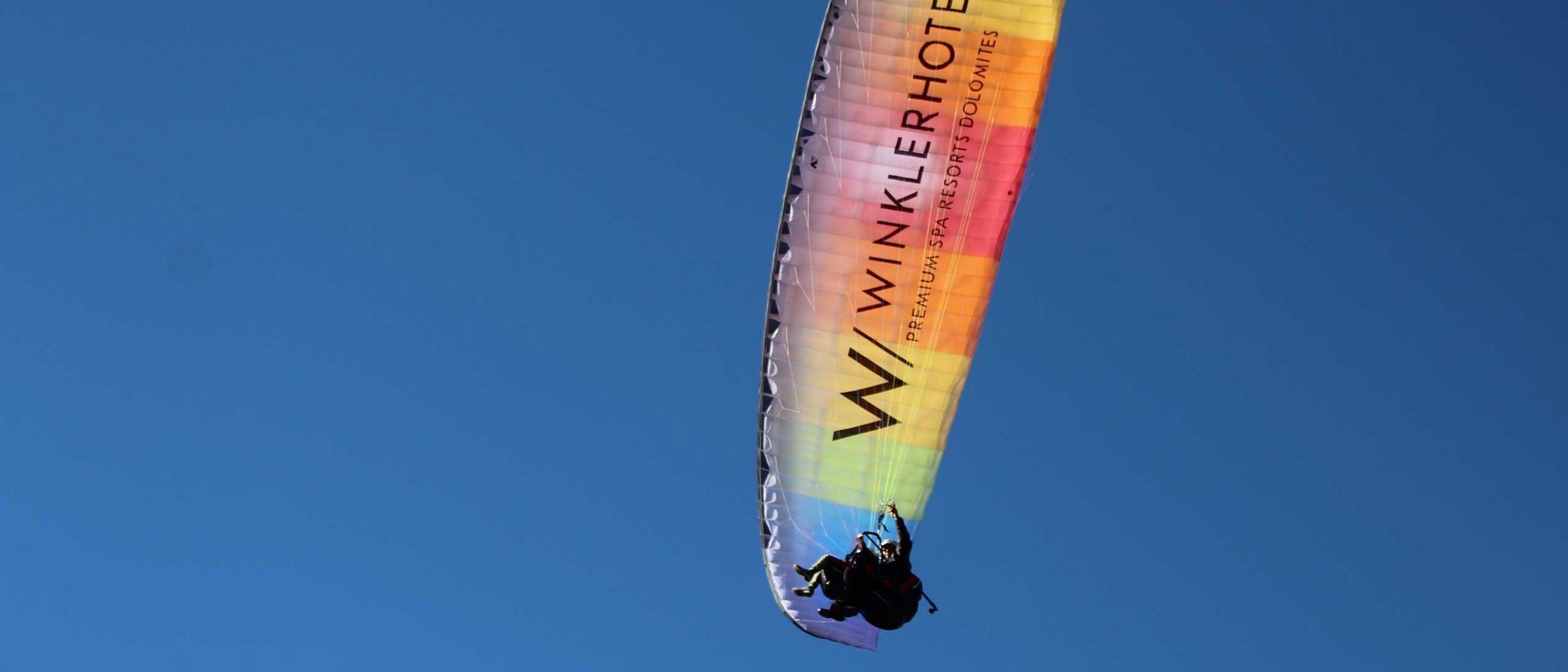 Außergewöhnliche Erlebnisse, Reiten und Yoga im Urlaub Zwei Personen Gleitschirmfliegen unter blauem Himmel mit farbigem Schirm