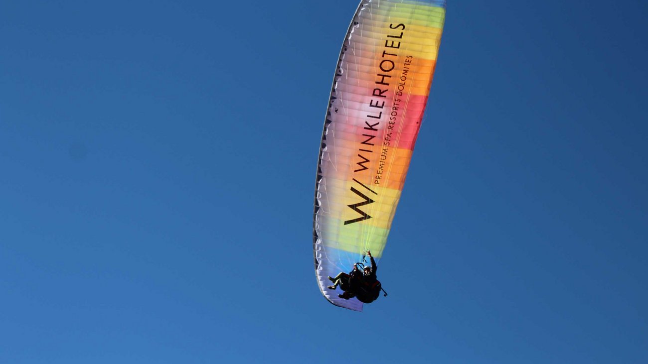 Außergewöhnliche Erlebnisse, Reiten und Yoga im Urlaub Zwei Personen Gleitschirmfliegen unter blauem Himmel mit farbigem Schirm