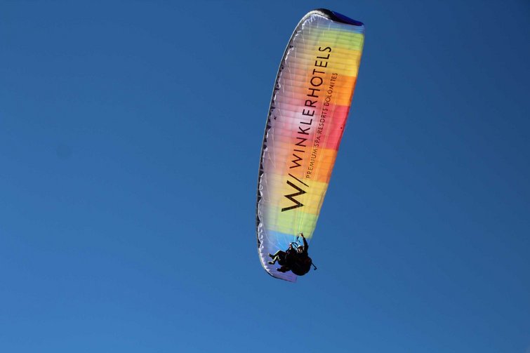 Due persone in parapendio sotto un cielo blu con vela colorata