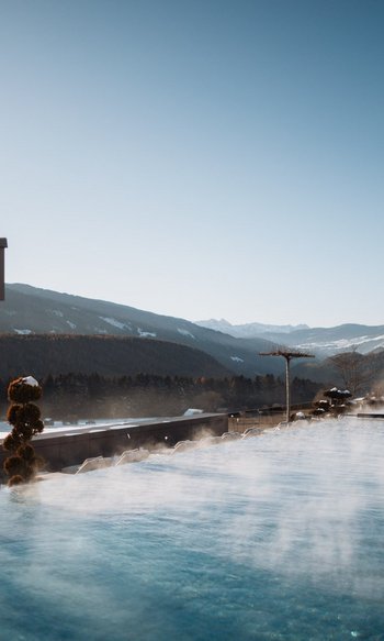 Your place to shine: our wellness hotel in South Tyrol Steaming outdoor pool with mountain view on a clear winter day
