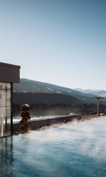 Die Heimat des Strahlens: Ihr Wellnesshotel in Südtirol Dampfender Außenpool mit Bergblick an einem klaren Wintertag