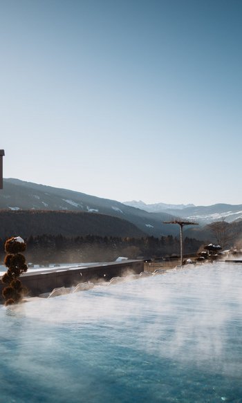 Piscina all'aperto fumante con vista sulle montagne in una giornata invernale limpida