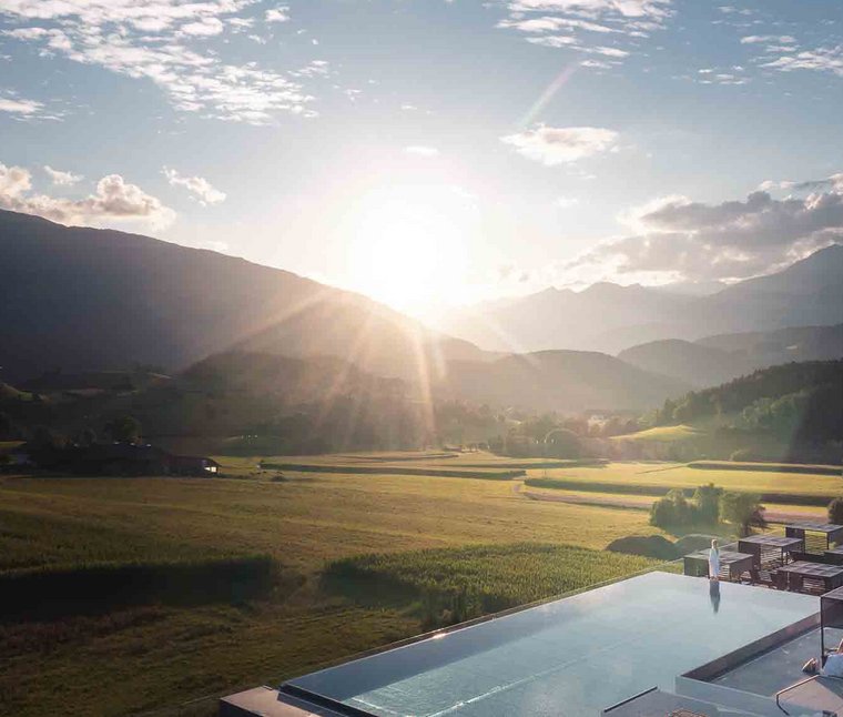 Ihre Hotels in Südtirol: die Heimat der Fülle Sonnenuntergang über Bergtal mit Feldern und Infinity-Pool