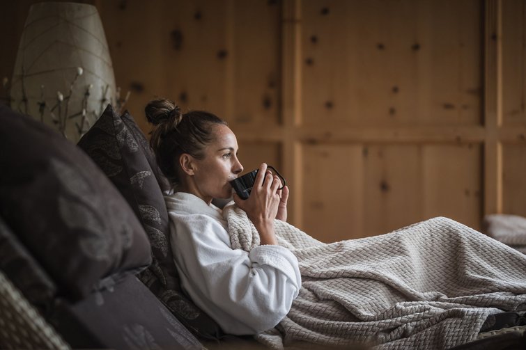 Frau in Bademantel trinkt Kaffee auf gemütlichem Sofa mit Decke