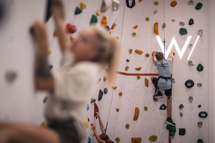 Bambini che scalano una parete da arrampicata in palestra