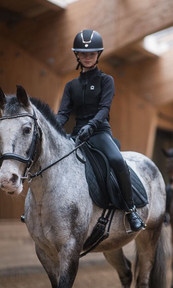 Giovane cavaliere su cavallo grigio in maneggio con un altro cavaliere sullo sfondo