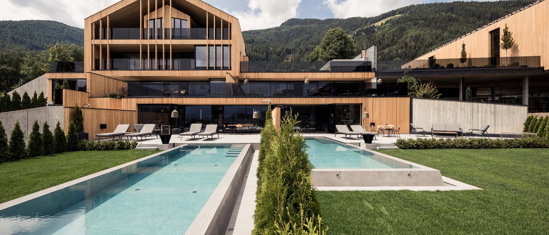 An enriching holiday in your luxury chalet in South Tyrol Modern wooden house with pool and loungers in front of forest and mountains