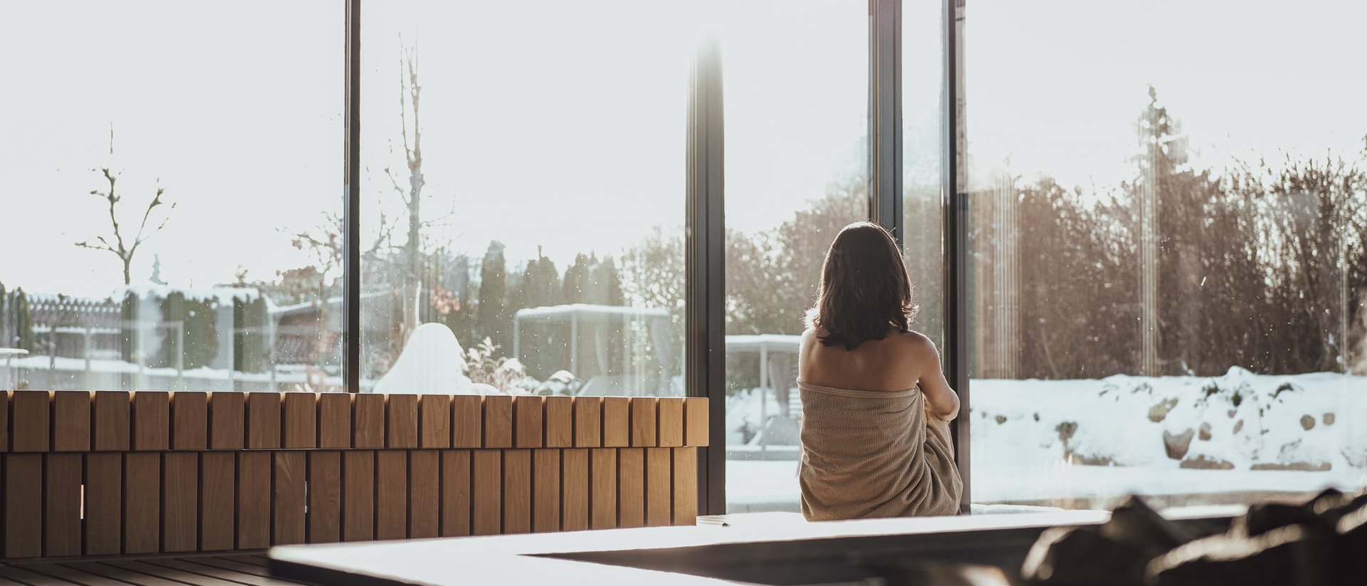 Frau in Sauna mit Blick auf verschneite Landschaft durch große Fenster
