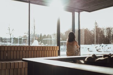 Frau in Sauna mit Blick auf verschneite Landschaft durch große Fenster