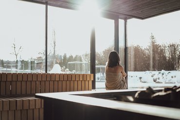 Eine regenerierende Auszeit vor Weihnachten Frau in Sauna mit Blick auf verschneite Landschaft durch große Fenster