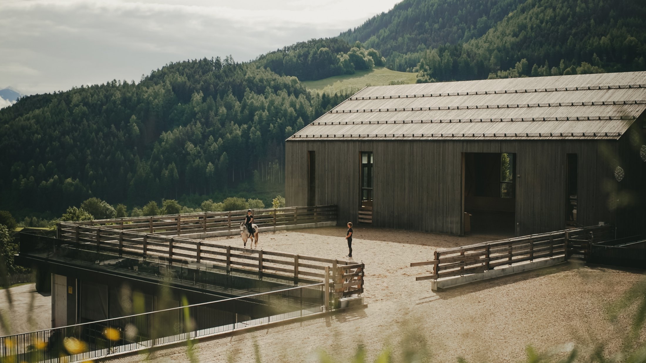 Maneggio con istruttore e studente a cavallo davanti a un capannone in montagna