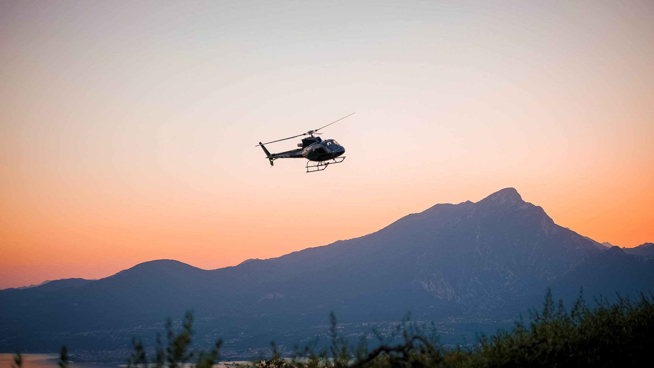 Elicottero vola al tramonto davanti a una catena montuosa