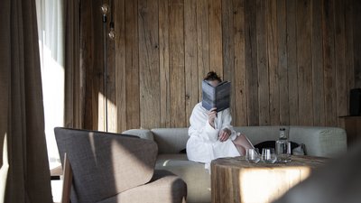 Persona in accappatoio legge su divano in salotto con parete in legno