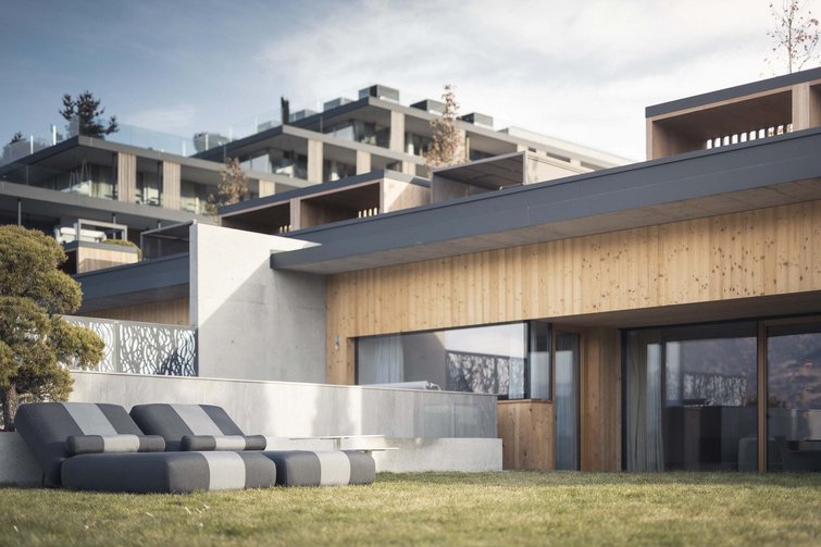 Modern patio with four padded lounge chairs in front of wooden house and lawn