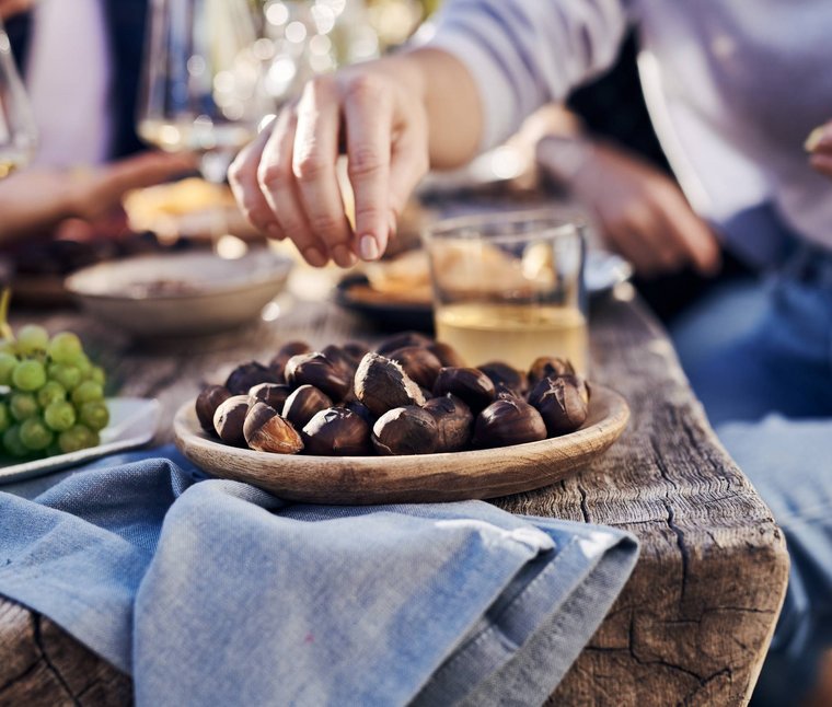 Winkler’s Stories: i nostri alberghi con maneggio di cavalli Mano che prende castagne arrostite da un piatto di legno su tavolo rustico