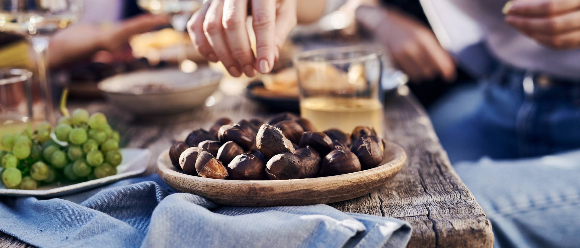 Die Tradition des Törggelens Hand nimmt geröstete Kastanien von einem Holzteller auf rustikalem Tisch