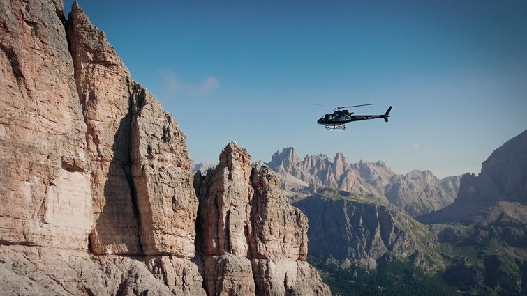 Elicottero vola sopra montagne rocciose con cielo sereno