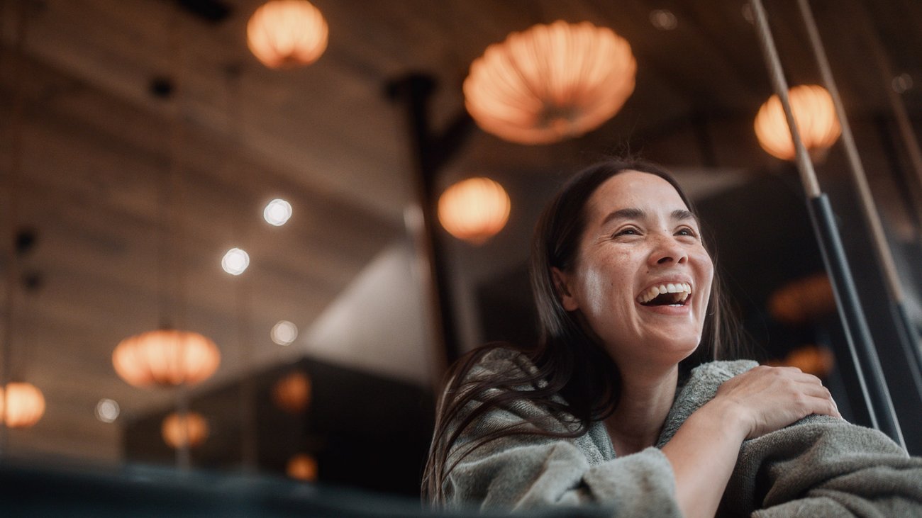 Frau lacht in gemütlichem Raum mit leuchtenden Lampen im Hintergrund