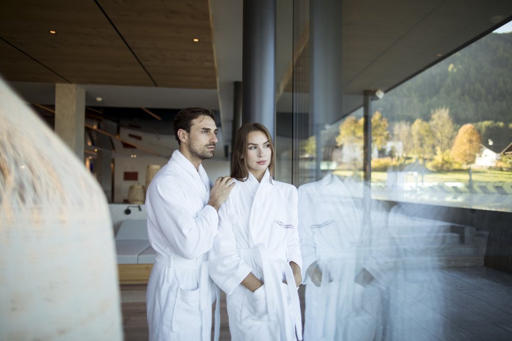 Paar in weißen Bademänteln blickt aus Panoramafenster im Spa