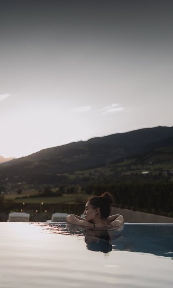 Die Heimat des Strahlens: Ihr Wellnesshotel in Südtirol Frau entspannt im Pool mit Bergblick bei Sonnenuntergang