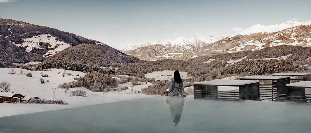 Der facettenreiche Spa unseres Spa-Hotels in Südtirol Person sitzt am Rand eines beheizten Pools mit Blick auf verschneite Berge
