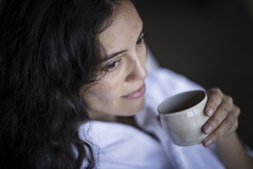 Donna con capelli scuri che beve da una tazza