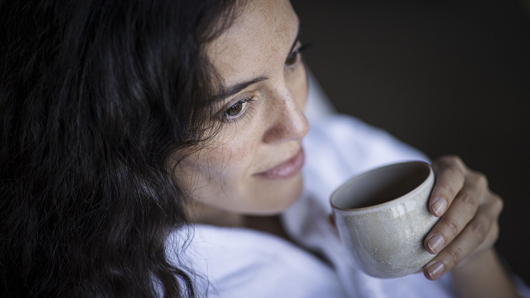Woman with dark hair holding and drinking from a cup