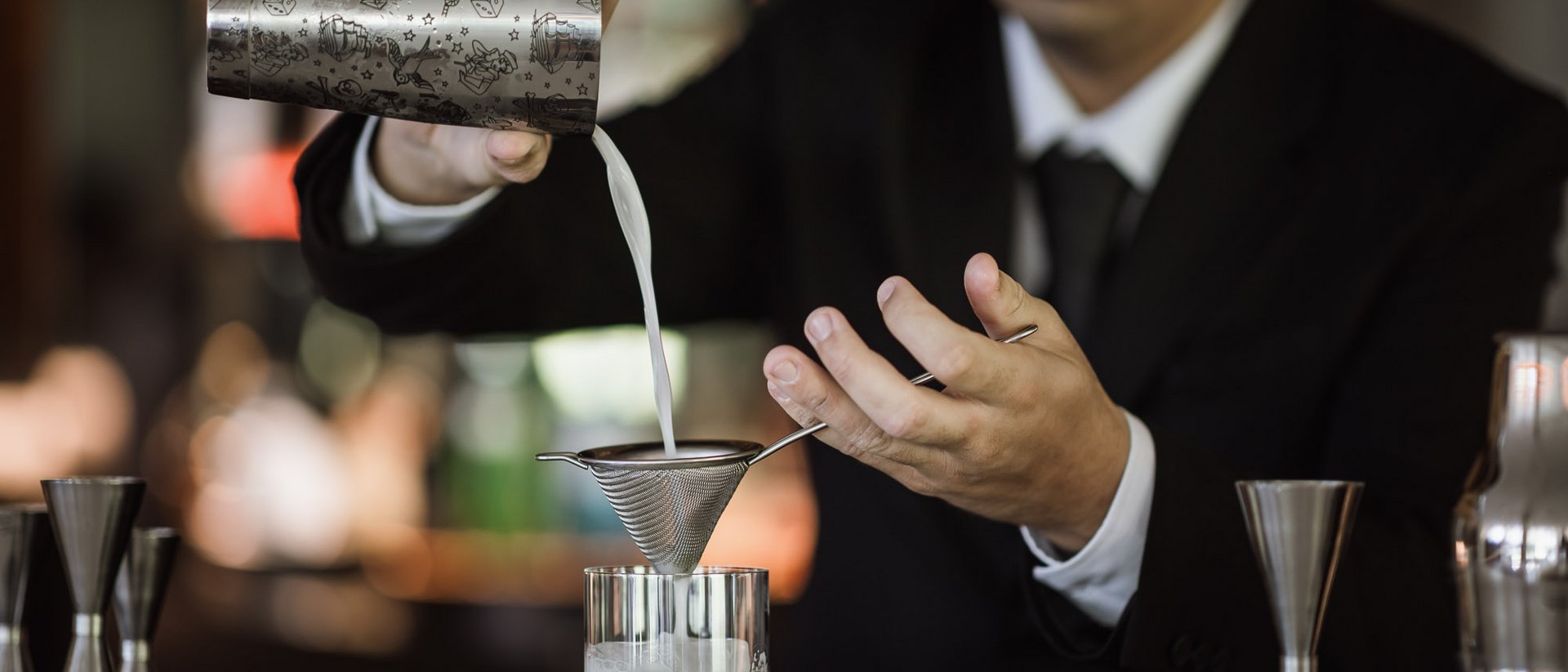 Barman filtra un liquido in un bicchiere usando un colino fine