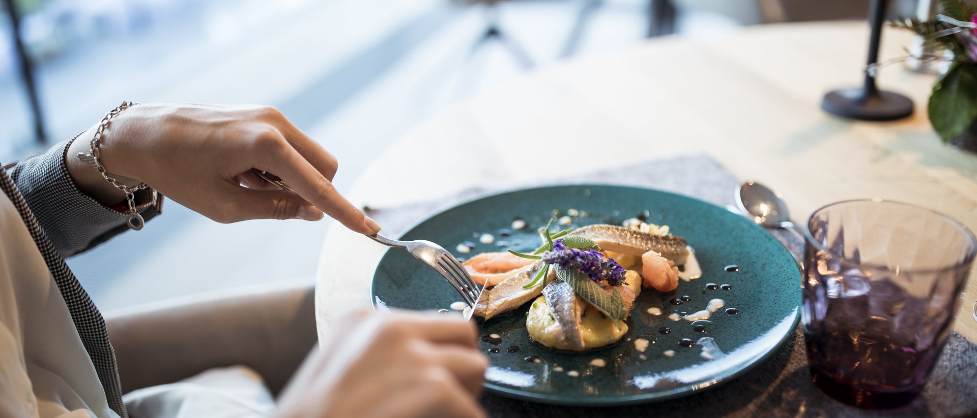 Person schneidet delikaten Fischgang auf blauem Teller beim Essen