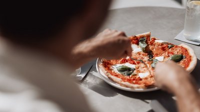 Person schneidet eine Pizza Margherita mit Basilikum auf einem Tisch