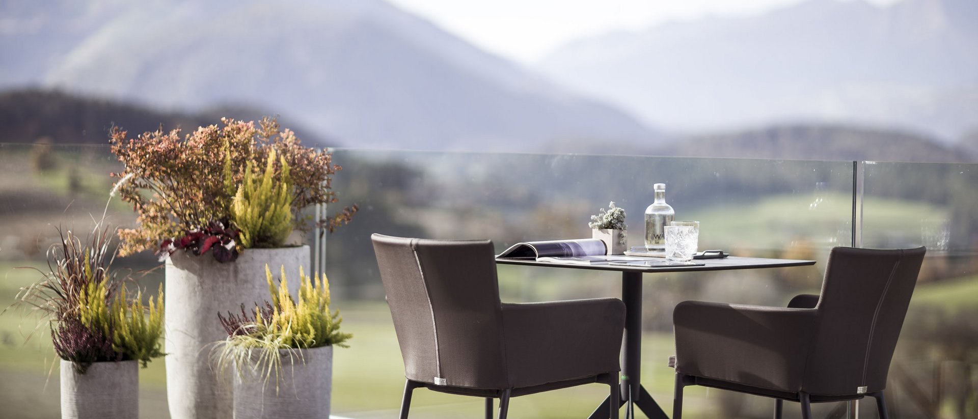 Terrassentisch mit zwei Stühlen und Blumen vor Berglandschaft