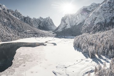 Verschneite Berglandschaft mit teilweise zugefrorenem See und Wäldern im Sonnenlicht