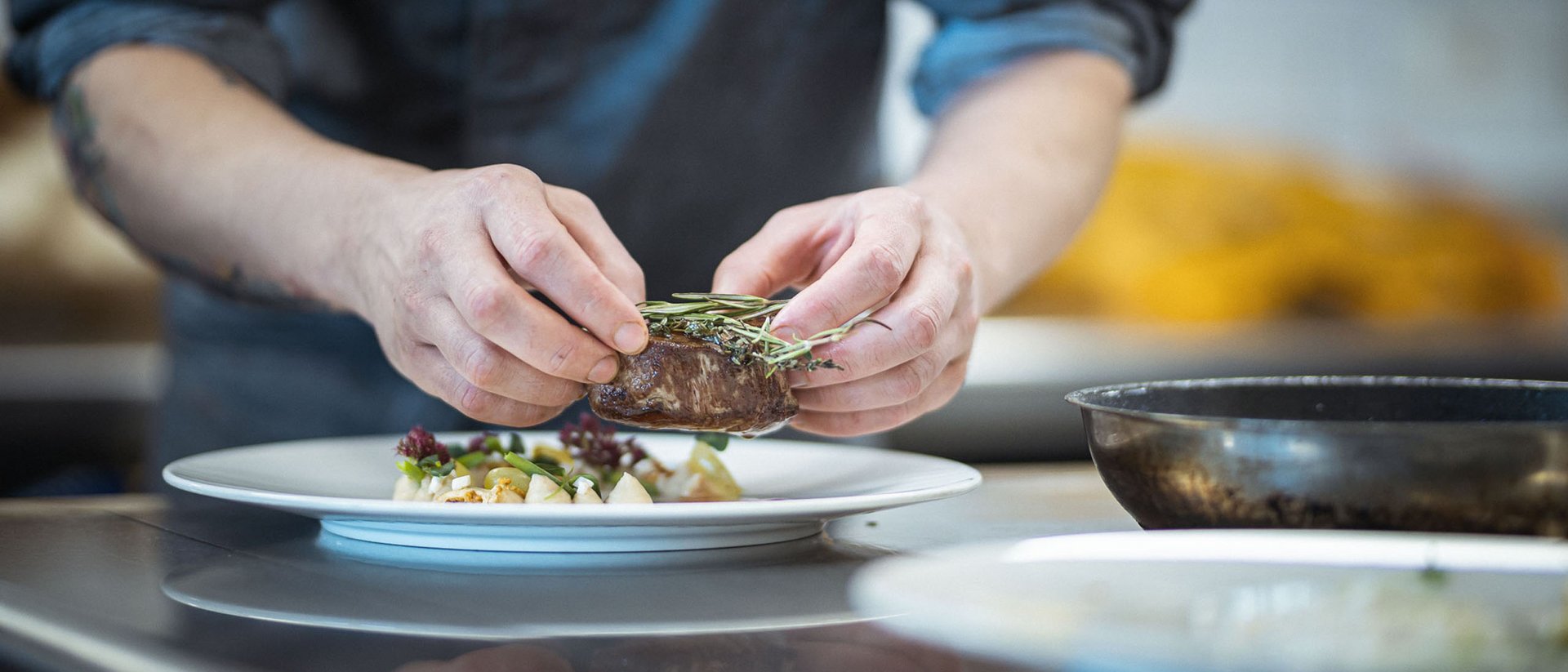 Chef plating tender steak with fresh herbs on a white plate