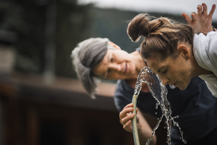 Frau wäscht ihr Gesicht mit Wasser aus Schlauch, eine weitere Frau schaut zu